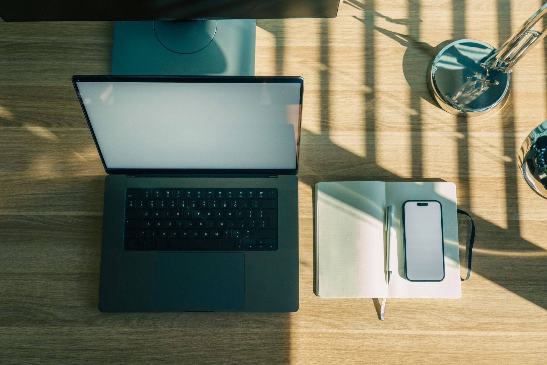 Minimal workspace with laptop, notebook and phone on a wooden desk in natural light