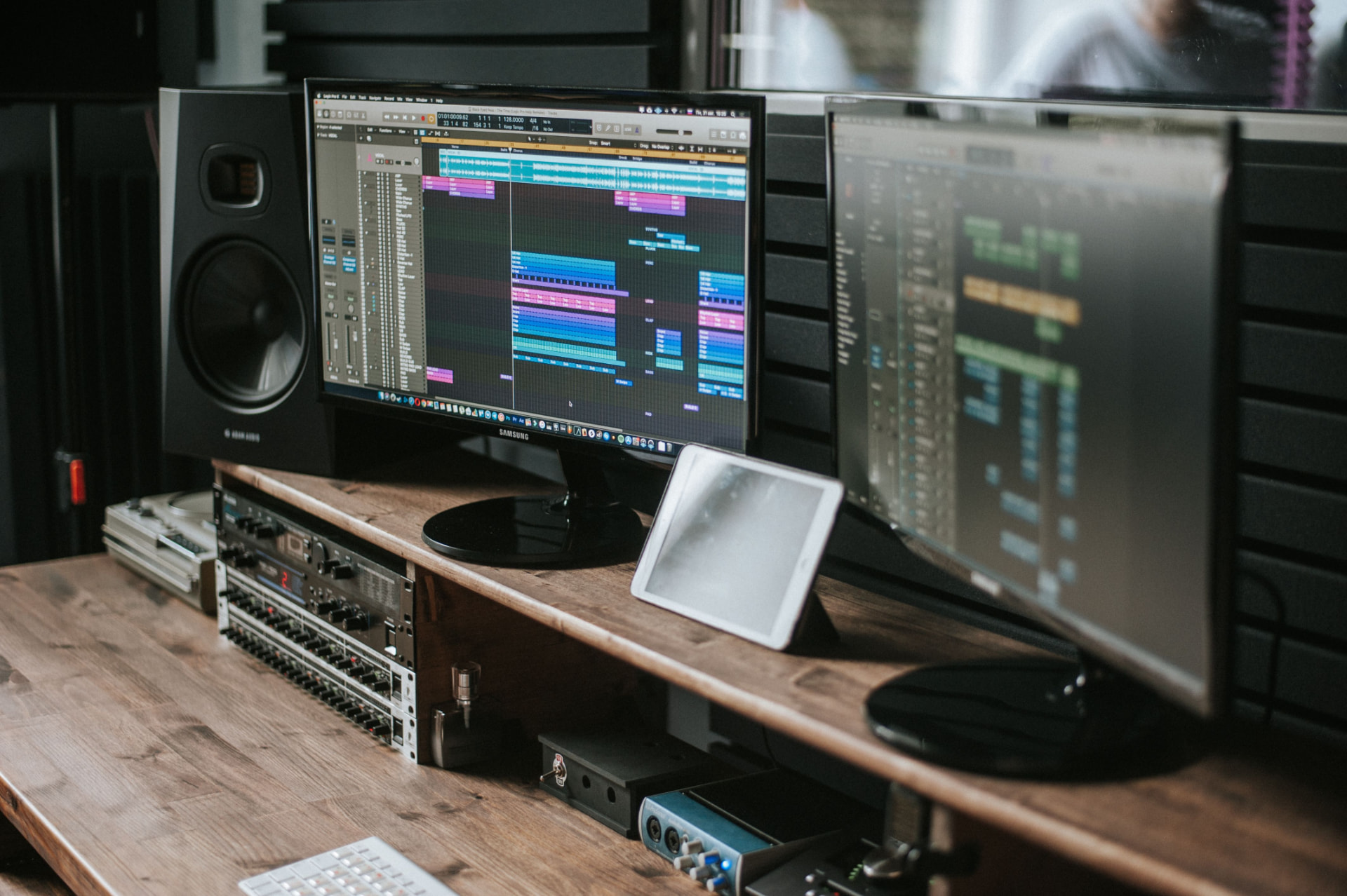 Dual-monitor studio desk running a DAW with tracks and mixing controls